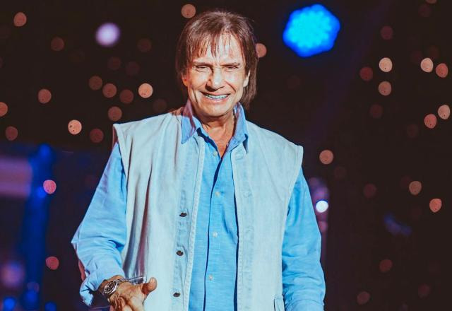 O cantor Roberto Carlos de terno azul, sorrindo em cima do palco durante show