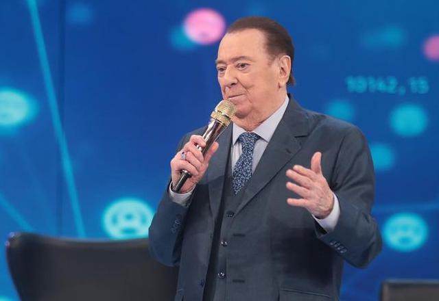 Raul Gil parado em pé no palco do Programa Raul Gil e segurando um microfone