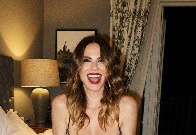 A apresentadora Luciana Gimenez posa sentada na cama, nua e sorrindo