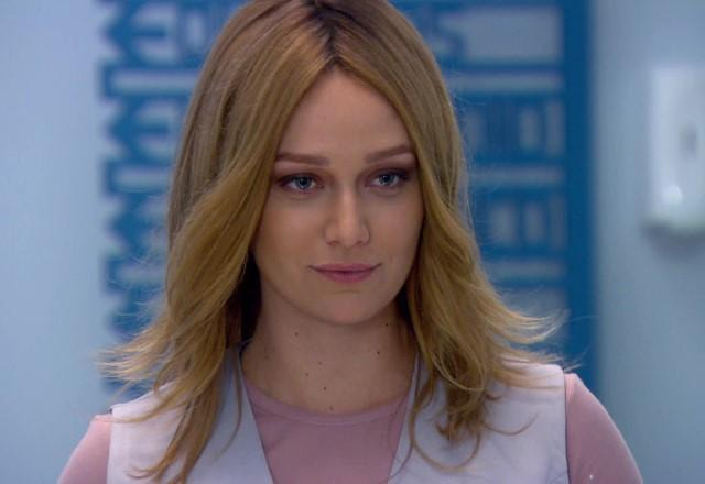Regina disfarçada com peruca loira e roupa de enfermeira, com uma expressão séria e má