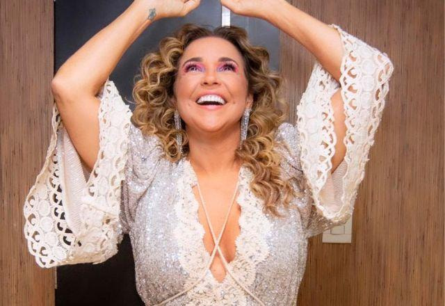 A cantora Daniela Mercury posa sorrindo e com as mãos para o alto