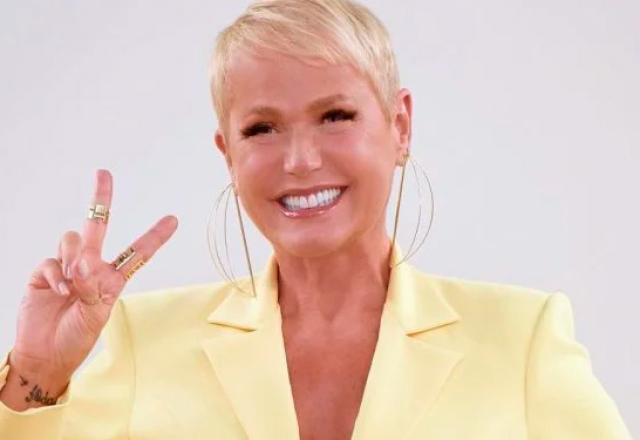 A apresentadora Xuxa Meneghel sorri e faz o número dois com as mãos