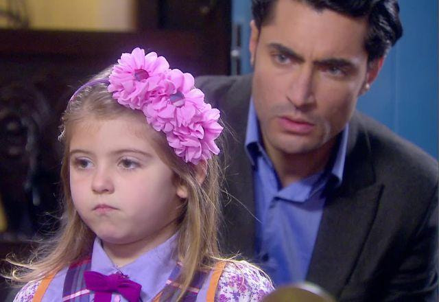 Dulce Maria aparece em primeiro plano com uma expressão séria e Gustavo aparece ao fundo um pouco desfocado e sério