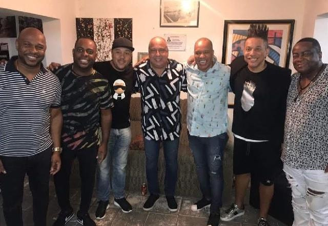 Integrantes da banda Molejo posam juntos, abraçados e sorrindo