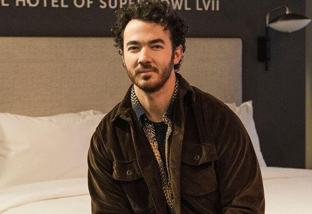 Kevin Jonas posa sentado na cama sorrindo