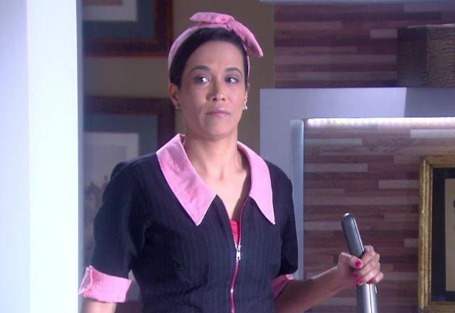 Franciely com uniforme, segurando um aspirador de pó na mão e ouvindo atrás da porta