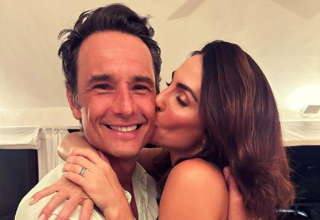 Rodrigo Santoro sendo beijado na bochecha por Mel Fronckowiak, que também está abraçando o marido