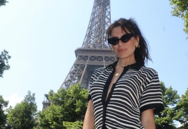 A modelo Mariana Goldfarb posando em frente a torre eiffel, vestida com uma blusa listrada, nas cores preto e branca