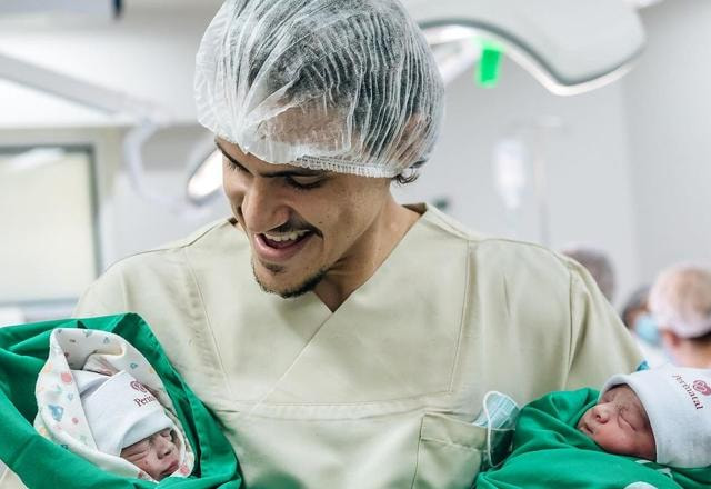 Foto de Pedro Guilherme segurando as duas filhas gêmeas