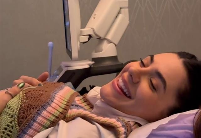 Foto de Jade Magalhães deitada com os olhos fechados e sorrindo durante o ultrassom de seu primeiro filho