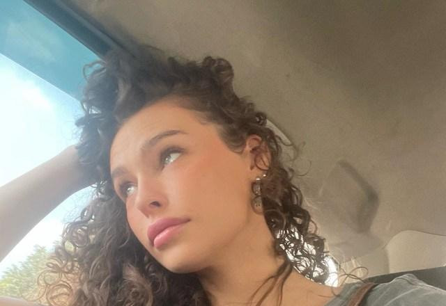 Foto da atriz Maidê Mahl, olhando pela janela de dentro de um carro