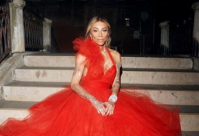 Imagem de Maya Massafera vestida com um vestido vermelho e posando para foto, sentada em uma escada, aparentemente na Itália