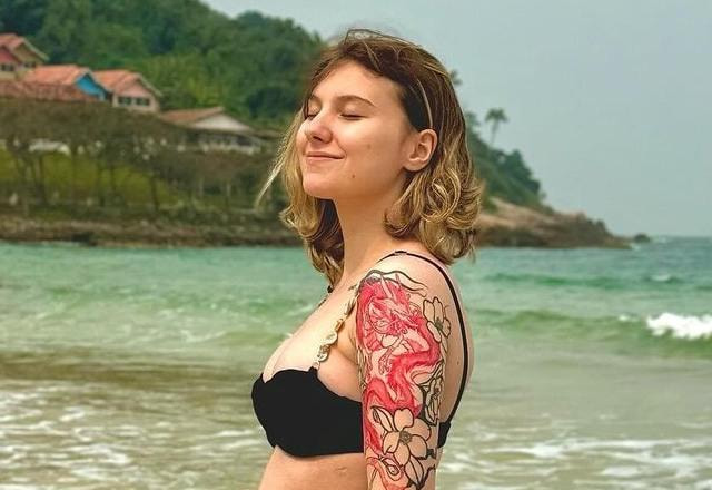 Foto de Isabel Veloso na praia de biquini sorrindo e com a mão em sua barriga, grávida de seu primeiro filho