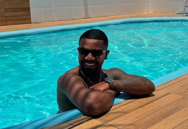 Foto de Davi Brito dentro de uma piscina, sorrindo, com óculos de sol no rosto