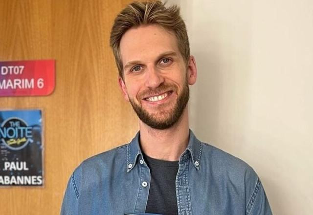 Foto de Paul Cabannes no camarim do programa do The Noite, de pé e segurando um copo