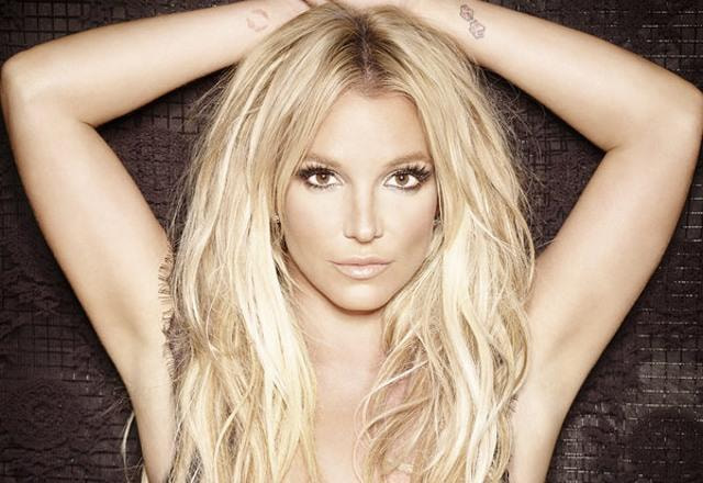 Foto de Britney Spears, maquiada e com as mão sobre a cabeça