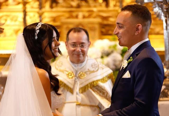 Foto de João Gomes e Ary Mirelle se casando, parados no altar olhando um para o outro, com um padre ao fundo