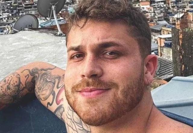 Foto de Gustavo Tubarão olhando para a câmera, sem camisa em um telhado de uma casa de periferia