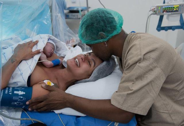 Carol Peixinho e Thiaguinho se abraçam com o filho recém-nascido nos braços.