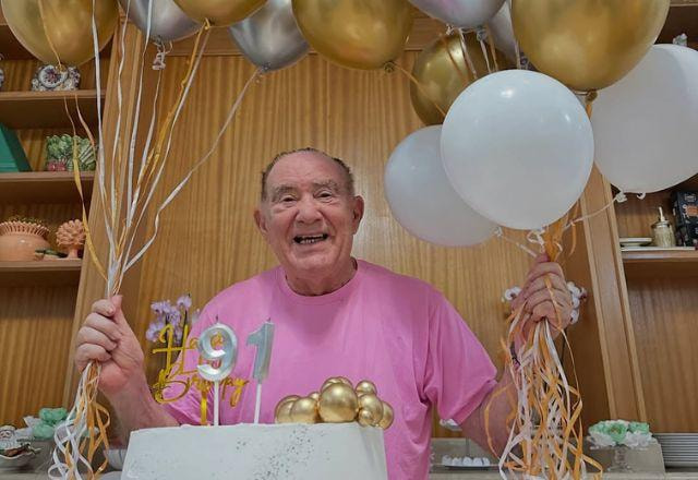 Renato Aragão posa com balões e bolo de 91 anos.