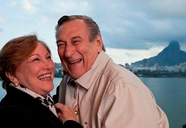 Nicette Bruno e Paulo Goulart, abraçados, sorriem para a foto, com a marina ao fundo